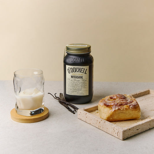 Vanilla Cream Moonshine 700ml Jar on a table with a cinnamon bun and glass filled with vanilla moonshine against a cream background