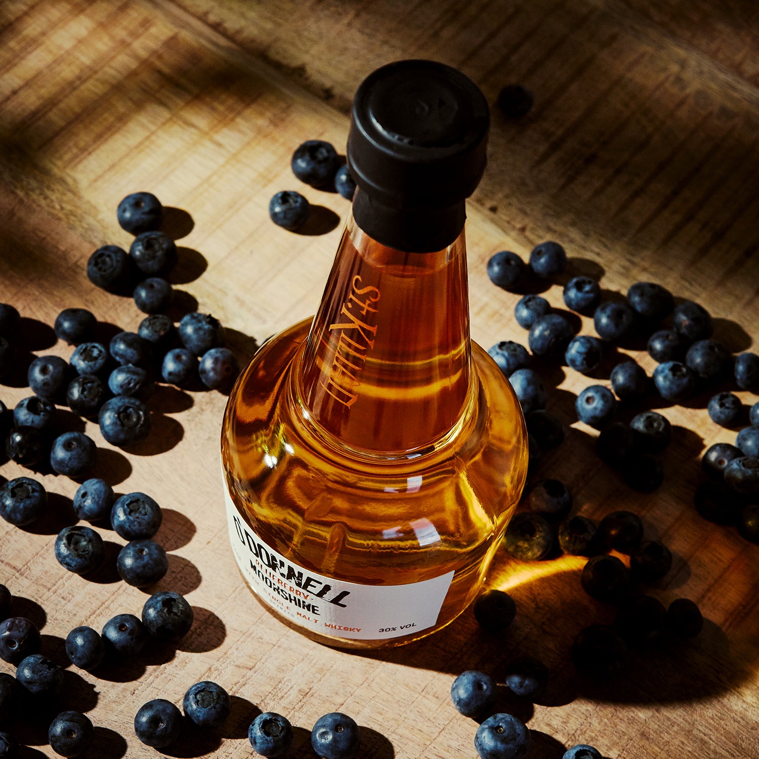 Bottle of st kilain and o'donnell moonshine whiskey surrounded by blueberries on a wooden surface