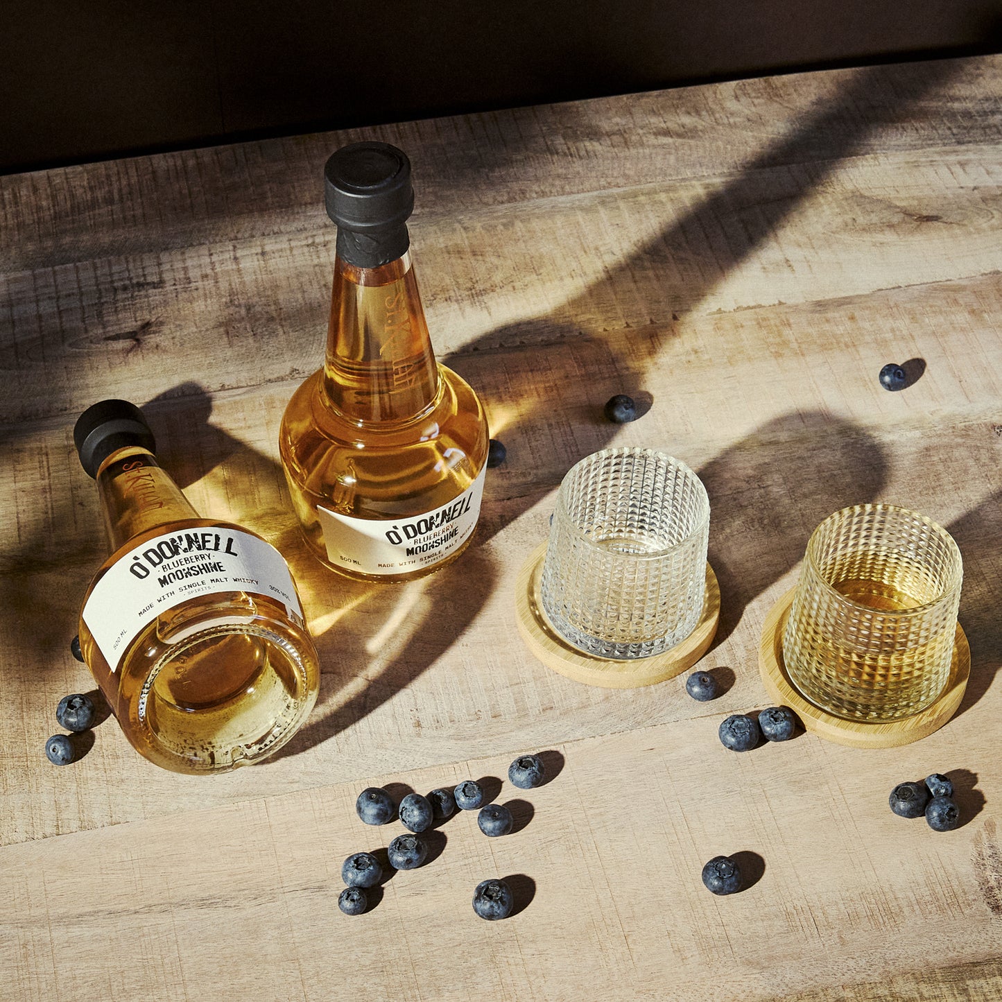 2 bottle of blueberry moonshine whisky with 2 glasses on a wooden surface