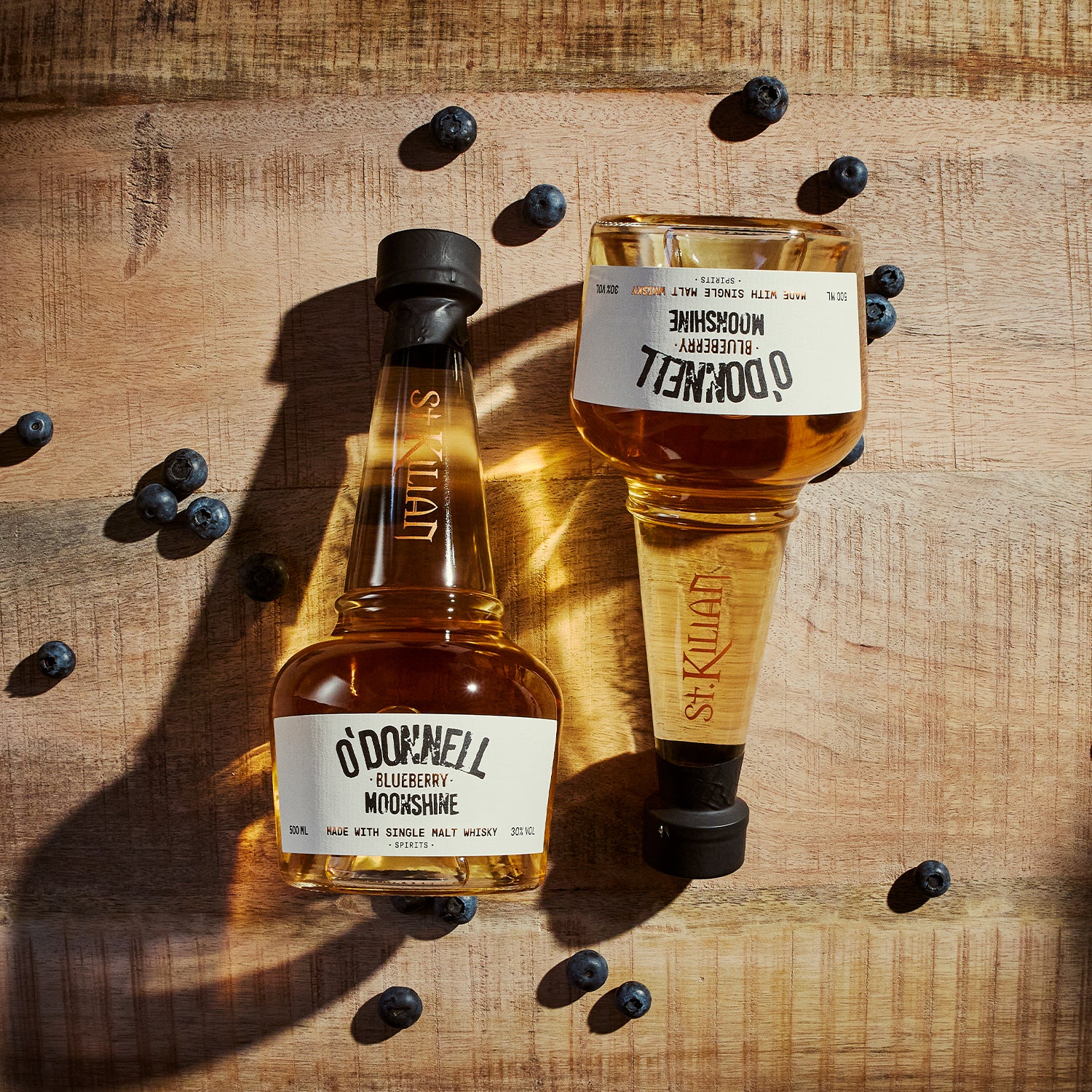 Two Bottles of O'Donnell moonshine on a wooden surface with blueberries.