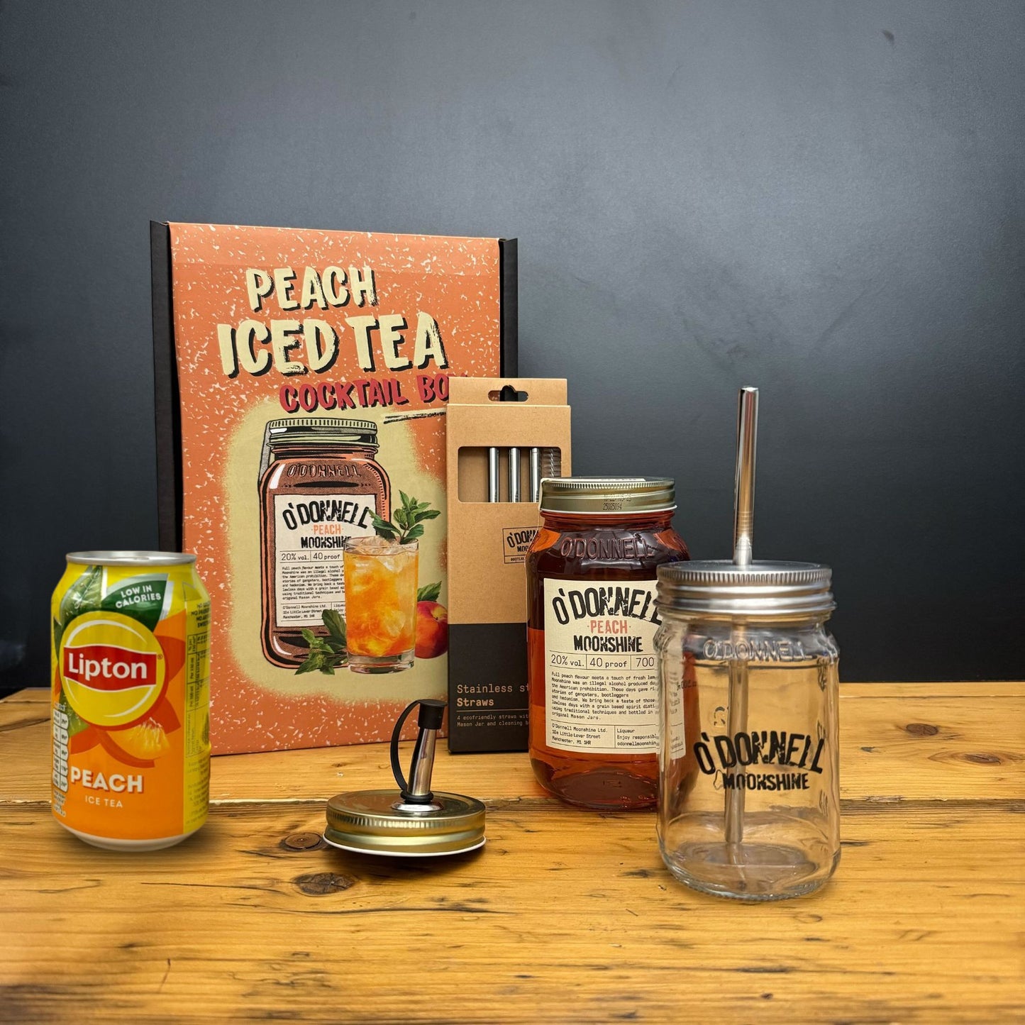 Peach iced tea can, jars with lids and straws, and a box on a wooden surface.
