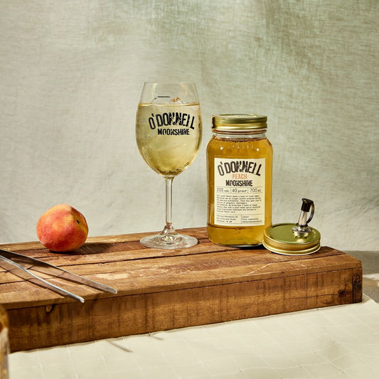 A Peach moonshine 700l Jar next to a O'Donnell Moonshine Spritz glass and a pouring lid.