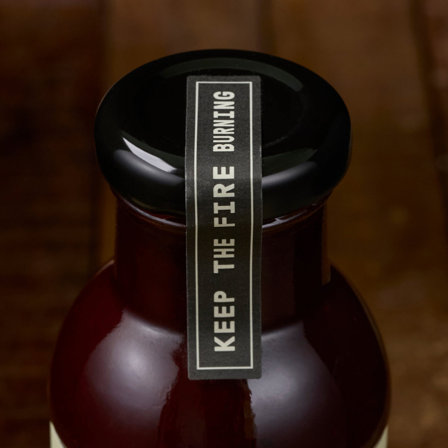 Bottle with a black cap and 'Keep the Fire Burning' label on a wooden background