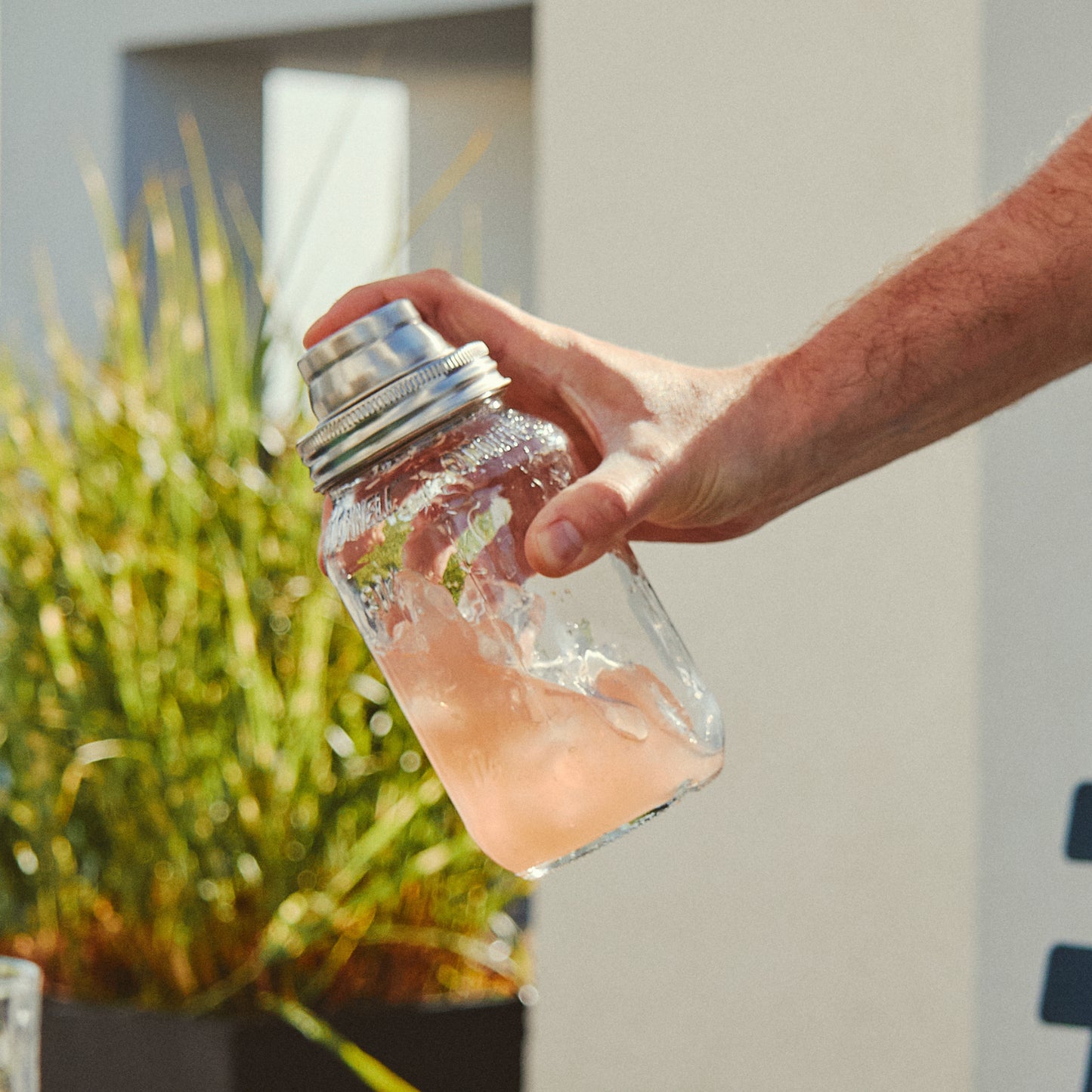 Hand holding a clear glass jar with a cocktail shaker lid attached