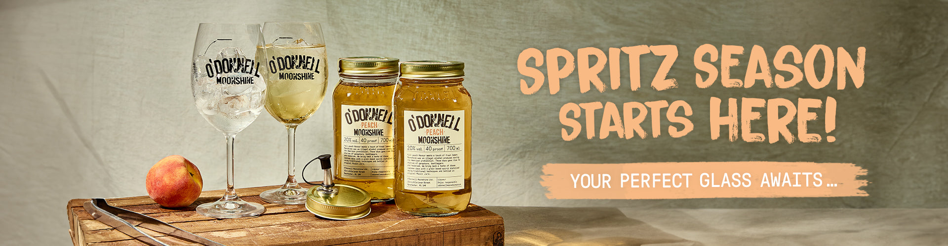 Spritz Season starts here. Your Perfect Glass Awaits, 2 peach moonshine jars, 2 spritz glasses and pouring lid on a wooden tray