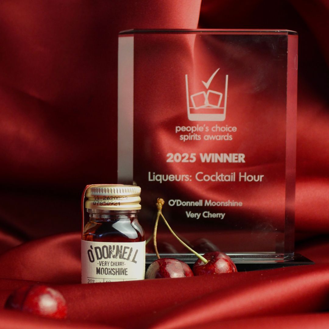 A glass award for '2025 Winner' in the 'Liqueurs: Cocktail Hour' category, placed next to a mini jar of O'Donnell Moonshine Very Cherry on a red background.