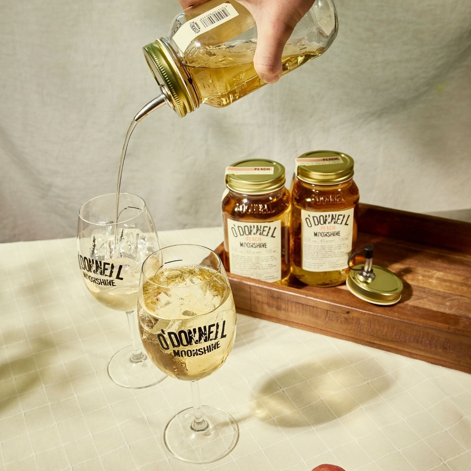 Two O'Donnell Sprit Glasses next to 2 700ml Jars of Peach Moonshine and a pouring lid. One is being poured