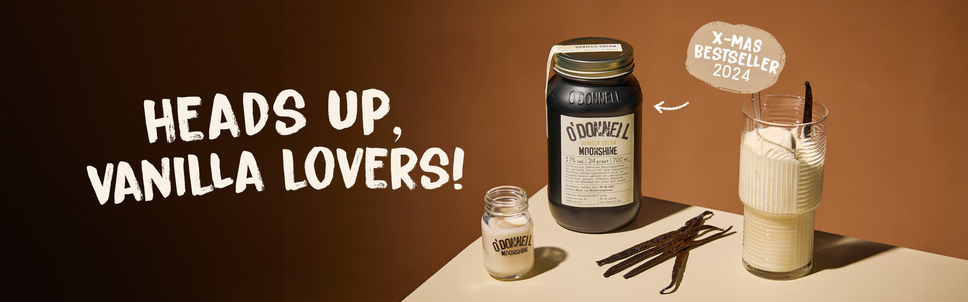 O'donnell vanilla cream moonshine jar against a brown background with a shot of moonshine and a vanilla filled glass with the text, Heads up vanilla lovers!