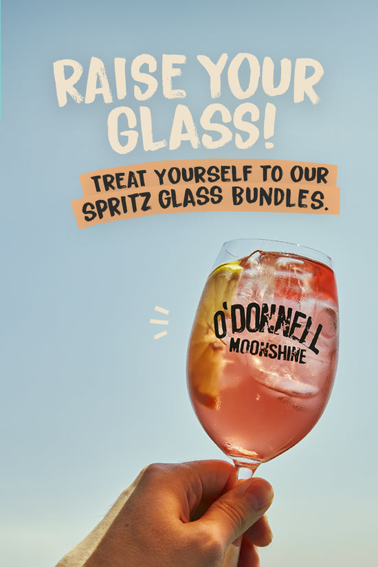 Raise your glass, shop spritz bundles. Image of a Spritz glass filled with a moonshine spritz against a blue background