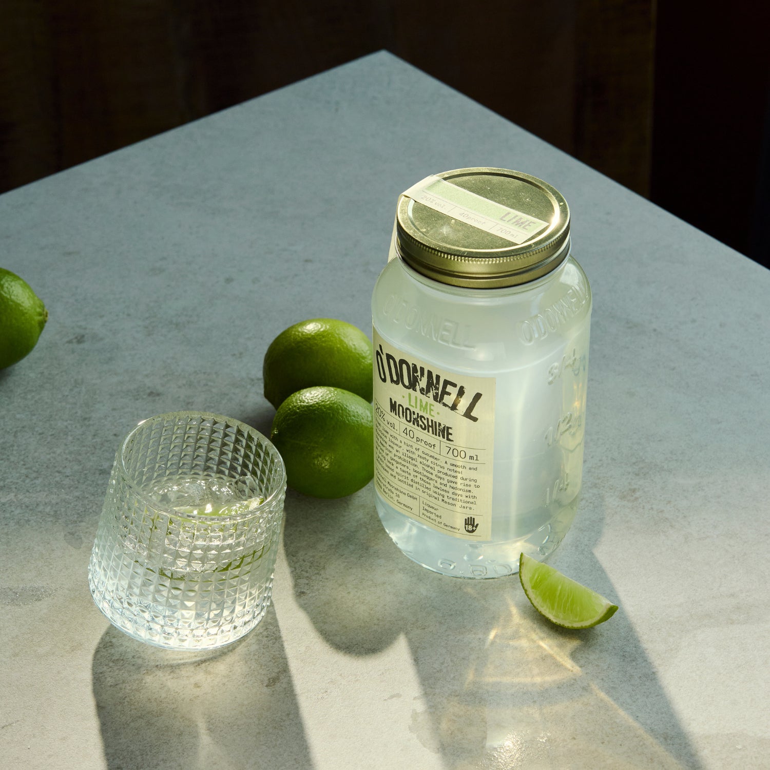 Jar of Lime Moonshine , glass, and limes on a grey surface