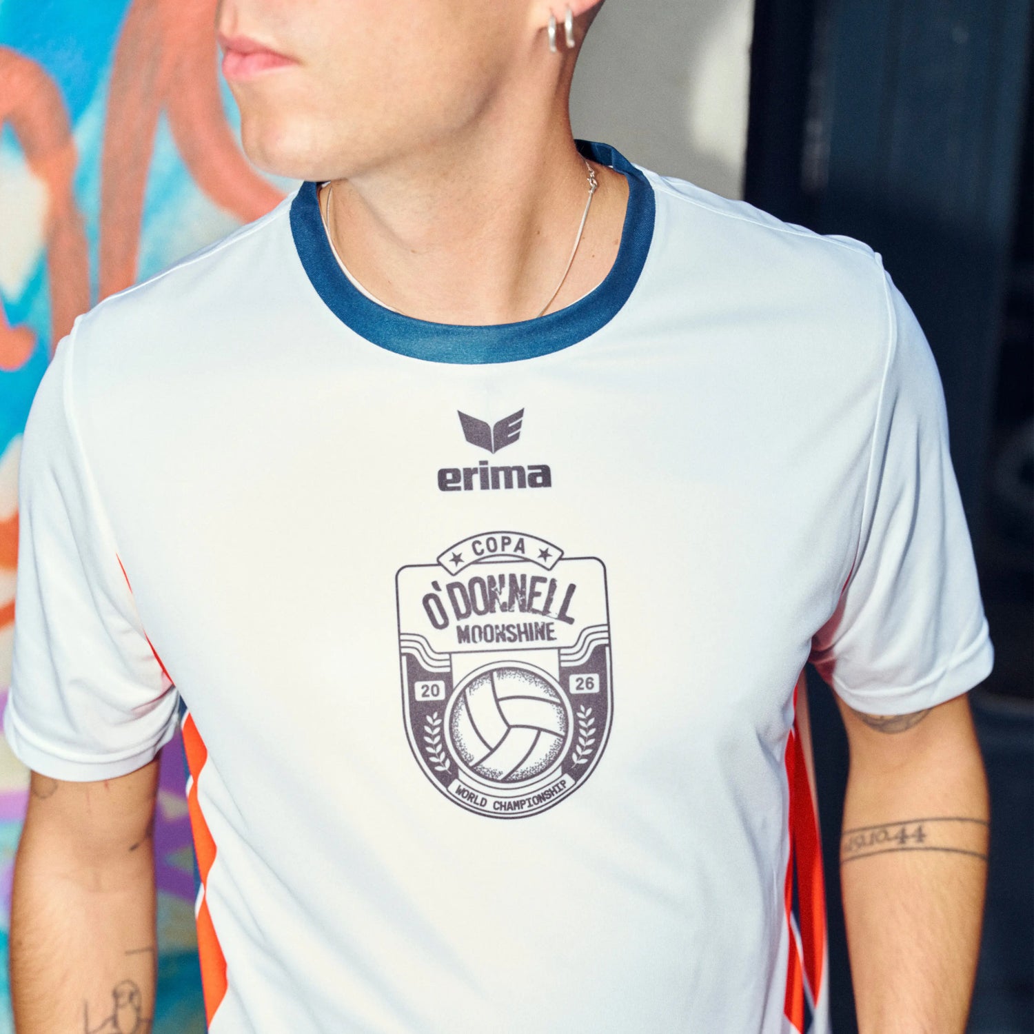 O'Donnell Moonshine WM Football Jersey – close-up of man wearing white jersey with Erima logo and Copa badge, orange side stripes, colourful street background