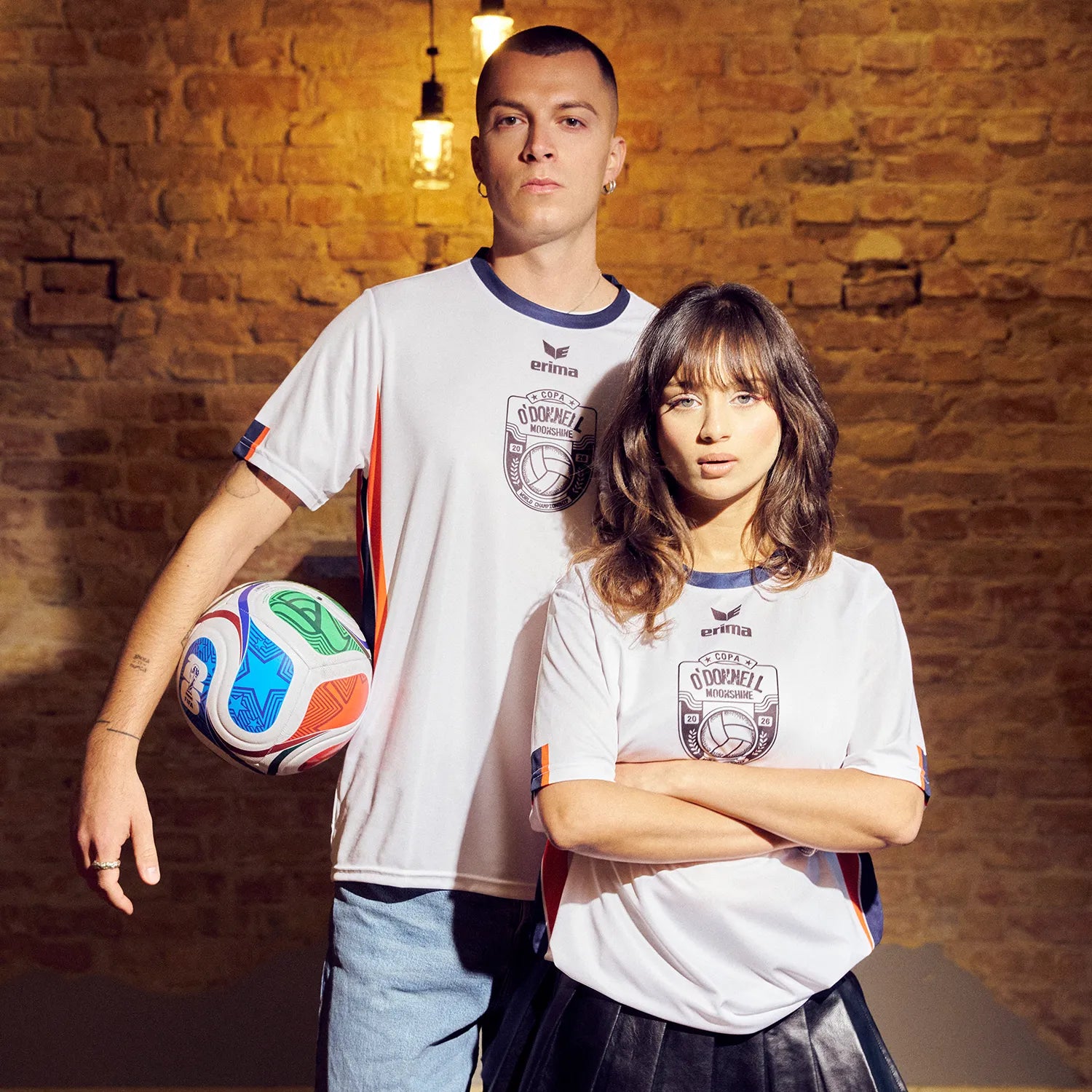 O'Donnell Moonshine WM Football Jersey – man and woman wearing matching white jerseys with Copa badge, man holding football, brick wall background