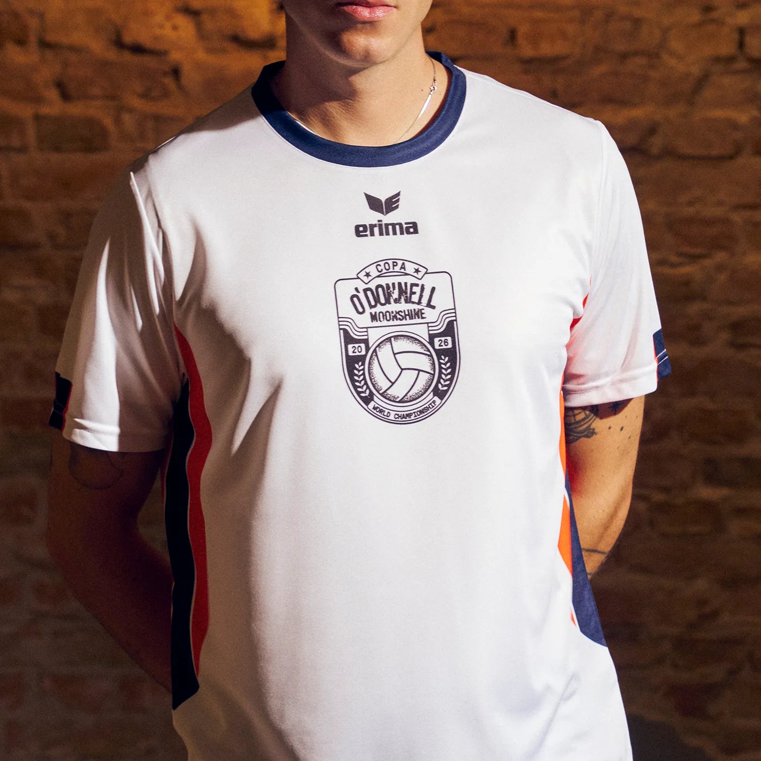 O'Donnell Moonshine WM Football Jersey – man wearing white jersey with Copa badge and orange side stripes, brick wall background