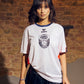 O'Donnell Moonshine WM Football Jersey – woman wearing white jersey with Copa badge and orange side stripes, brick wall background