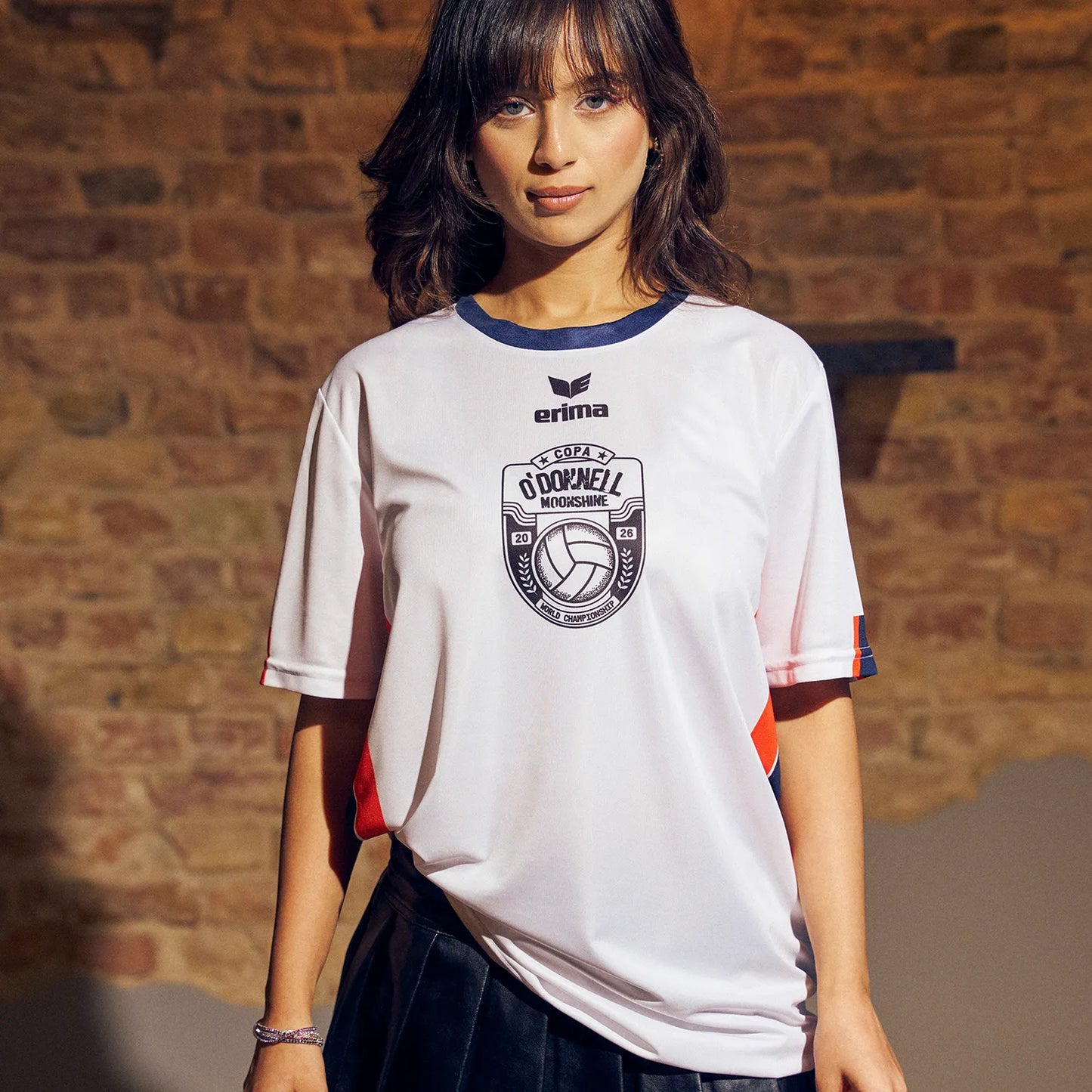 O'Donnell Moonshine WM Football Jersey – woman wearing white jersey with Copa badge and orange side stripes, brick wall background