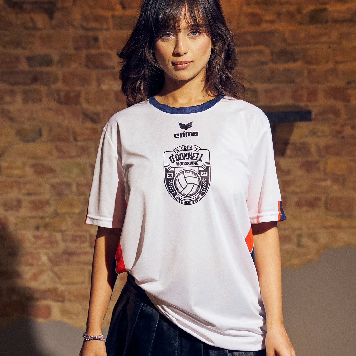 O'Donnell Moonshine WM Football Jersey – woman wearing white jersey with Copa badge and orange side stripes, brick wall background