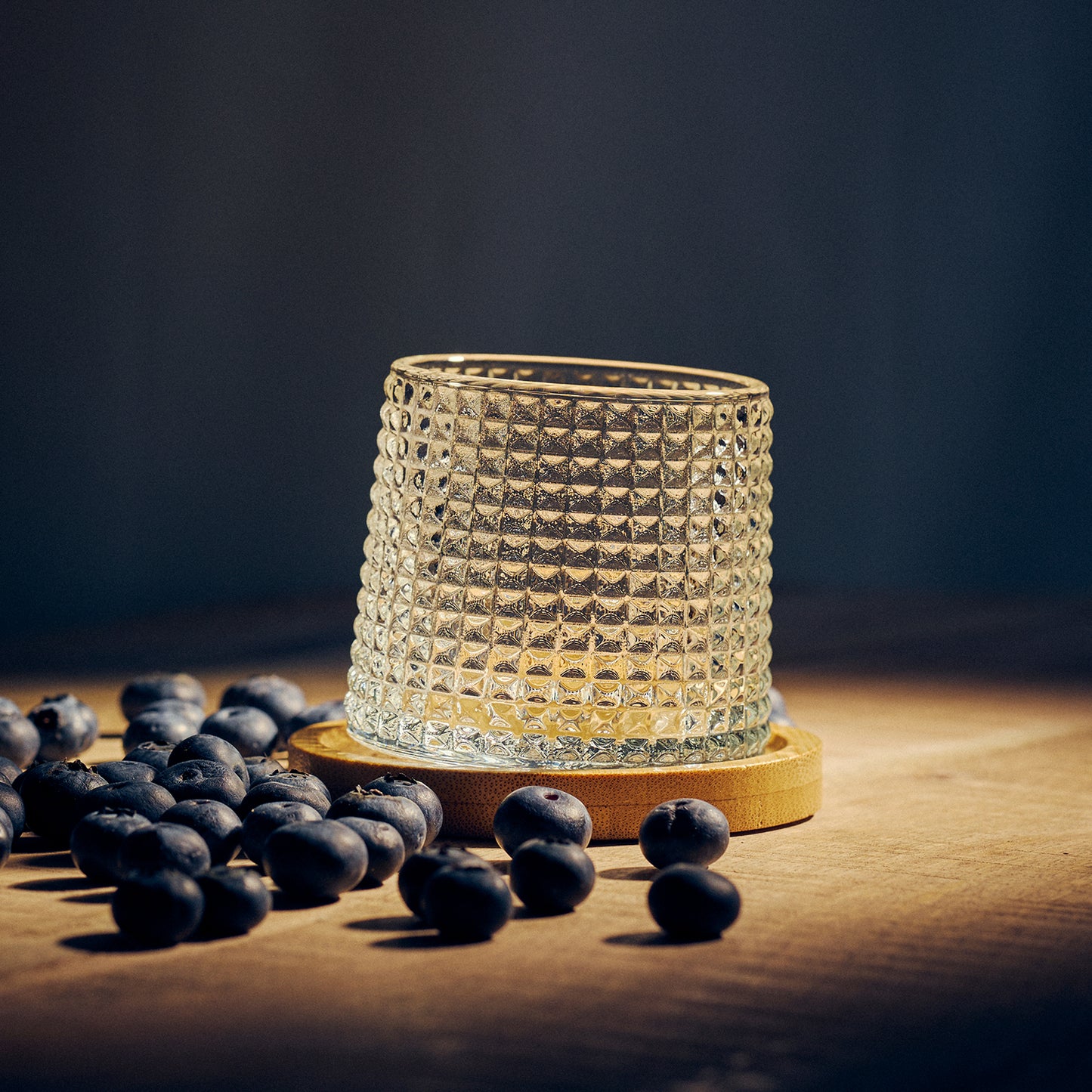 Textured Tumbler Glass on a wooden coaster. Surrounded by blueberries