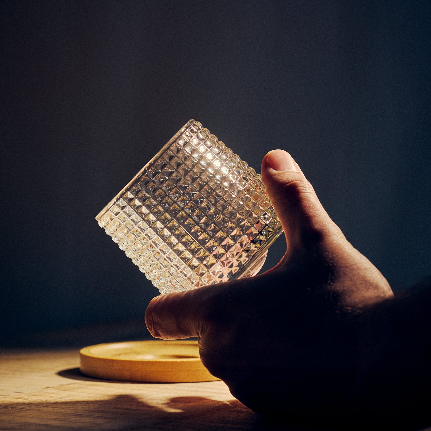 Hand holding a textured glass cup against a dark background