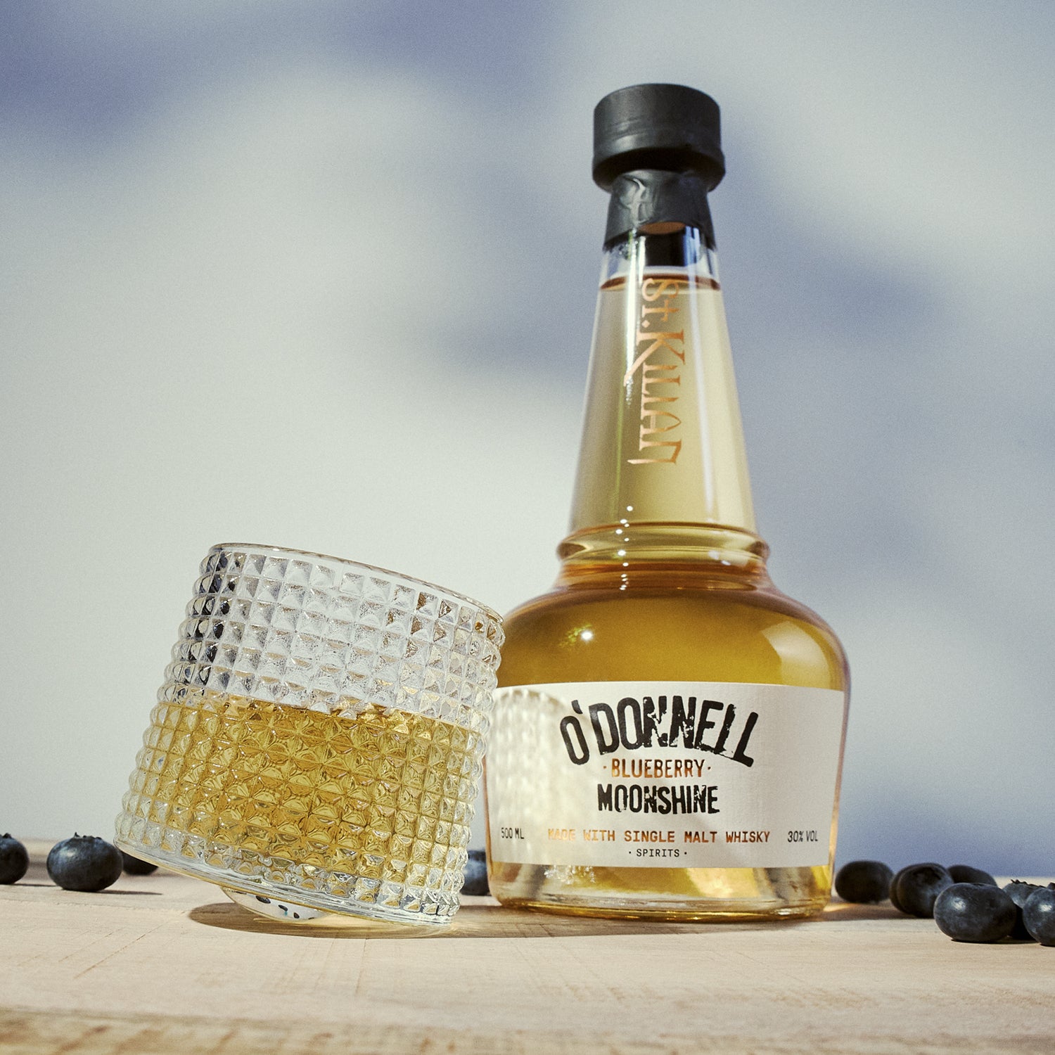 bottle of blueberry moonshine whisky with a glass on a wooden surface