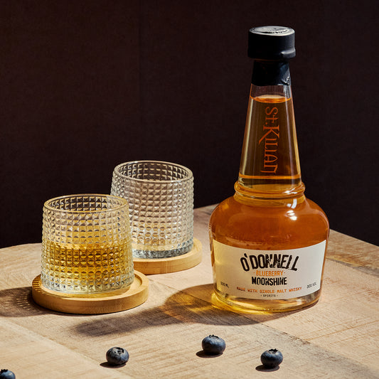 bottle of blueberry moonshine whisky with two glasses on a wooden surface