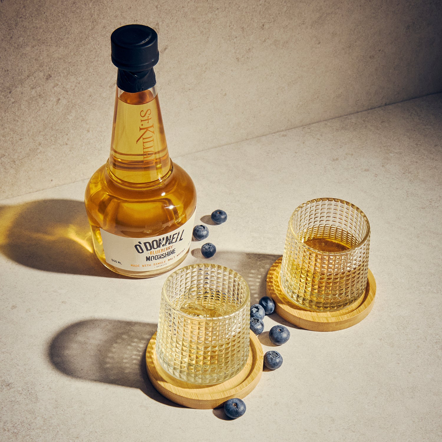 bottle of blueberry moonshine whisky with 2 glasses on a wooden surface
