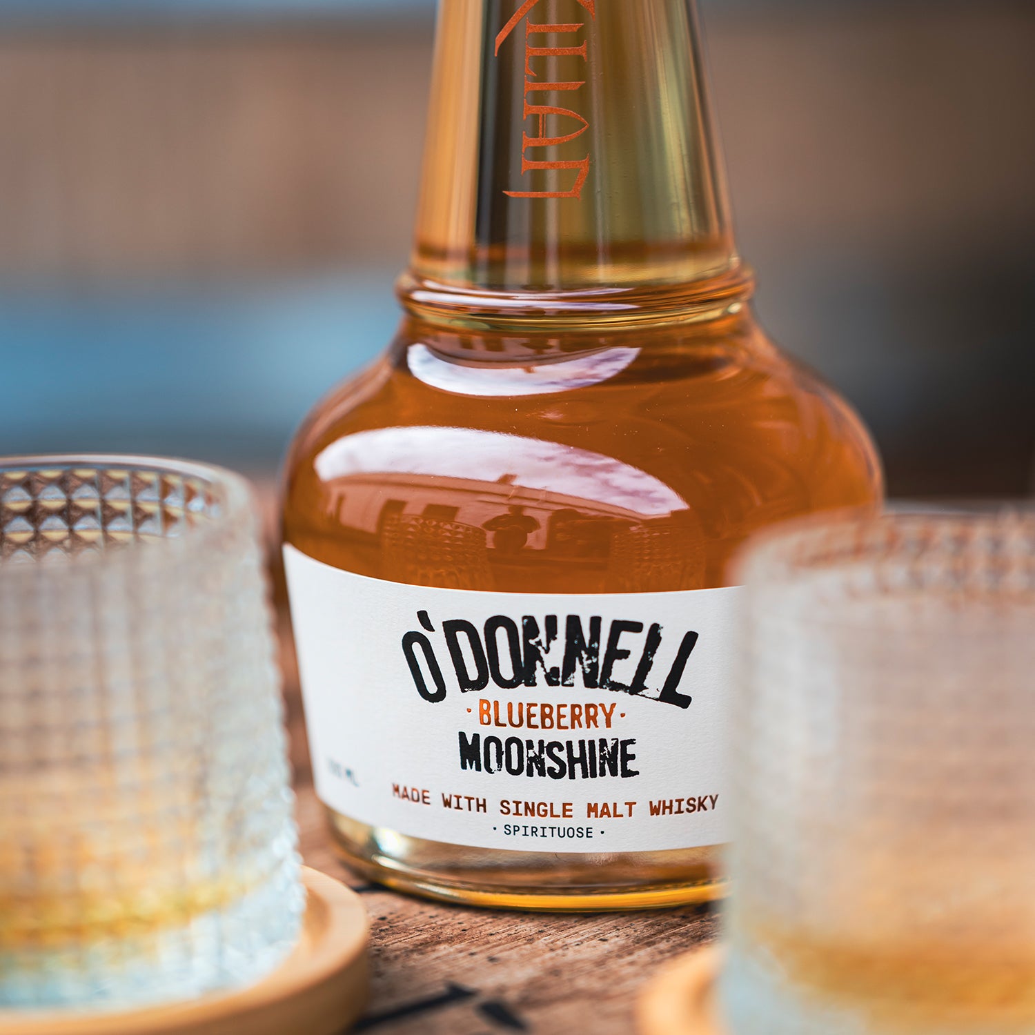 Bottle of O'Donnell Blueberry Moonshine with two glasses on a wooden surface.