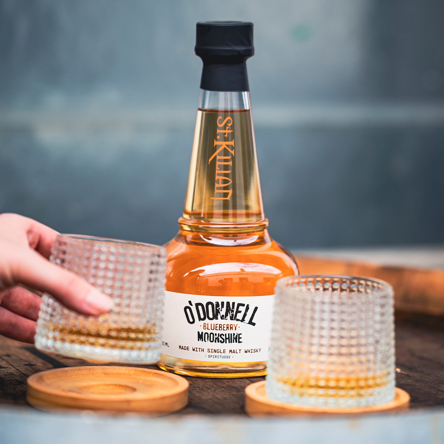 Bottle of O'Donnell Blueberry Moonshine with two glasses on a wooden surface.