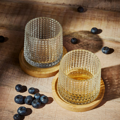 Two textured Tumbler Glasses on a wooden coaster. Surrounded by blueberries