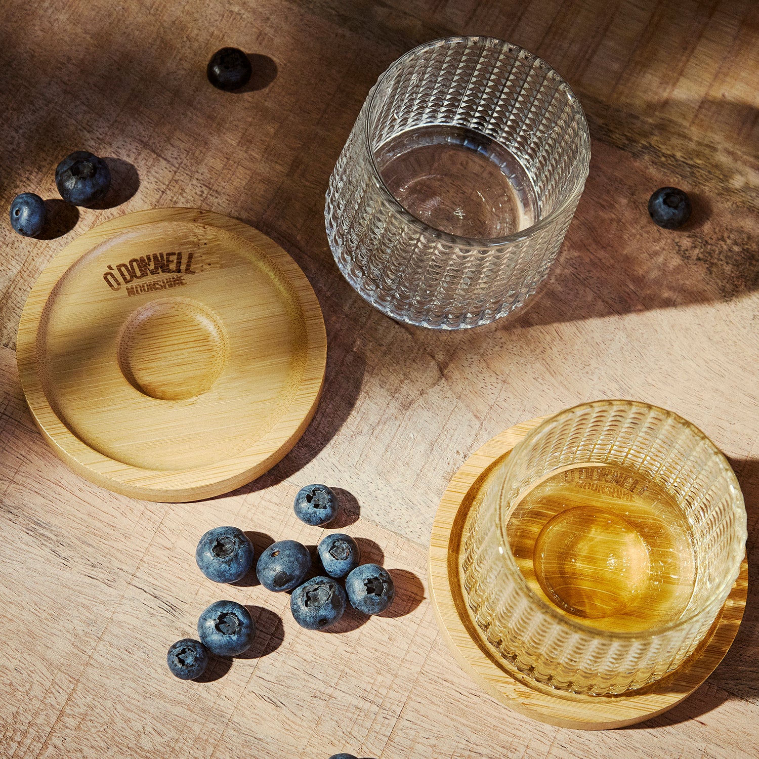 Two Textured Tumbler Glass on a wooden coaster. Surrounded by blueberries