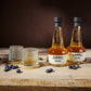 two bottles of blueberry moonshine whisky with a glass on a wooden surface
