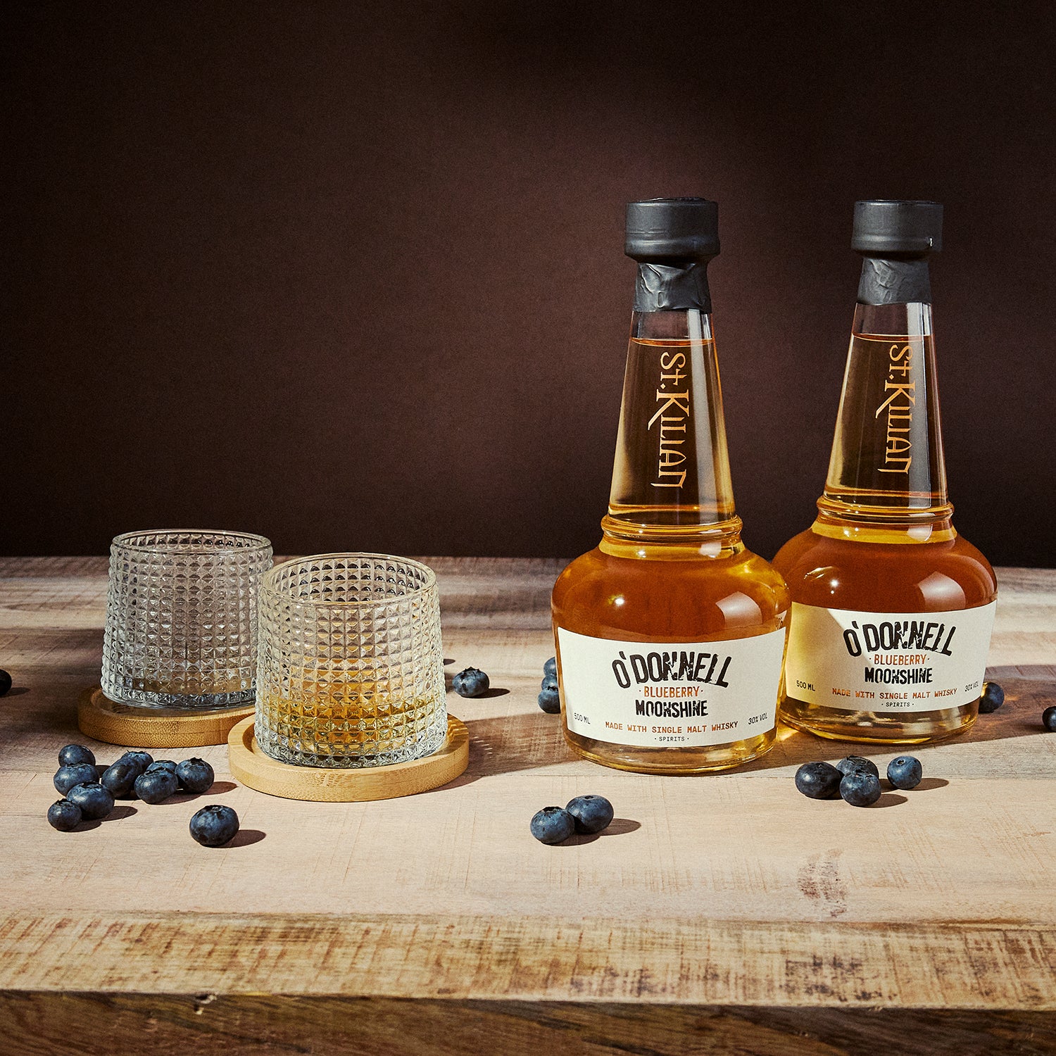 two bottles of blueberry moonshine whisky with a glass on a wooden surface
