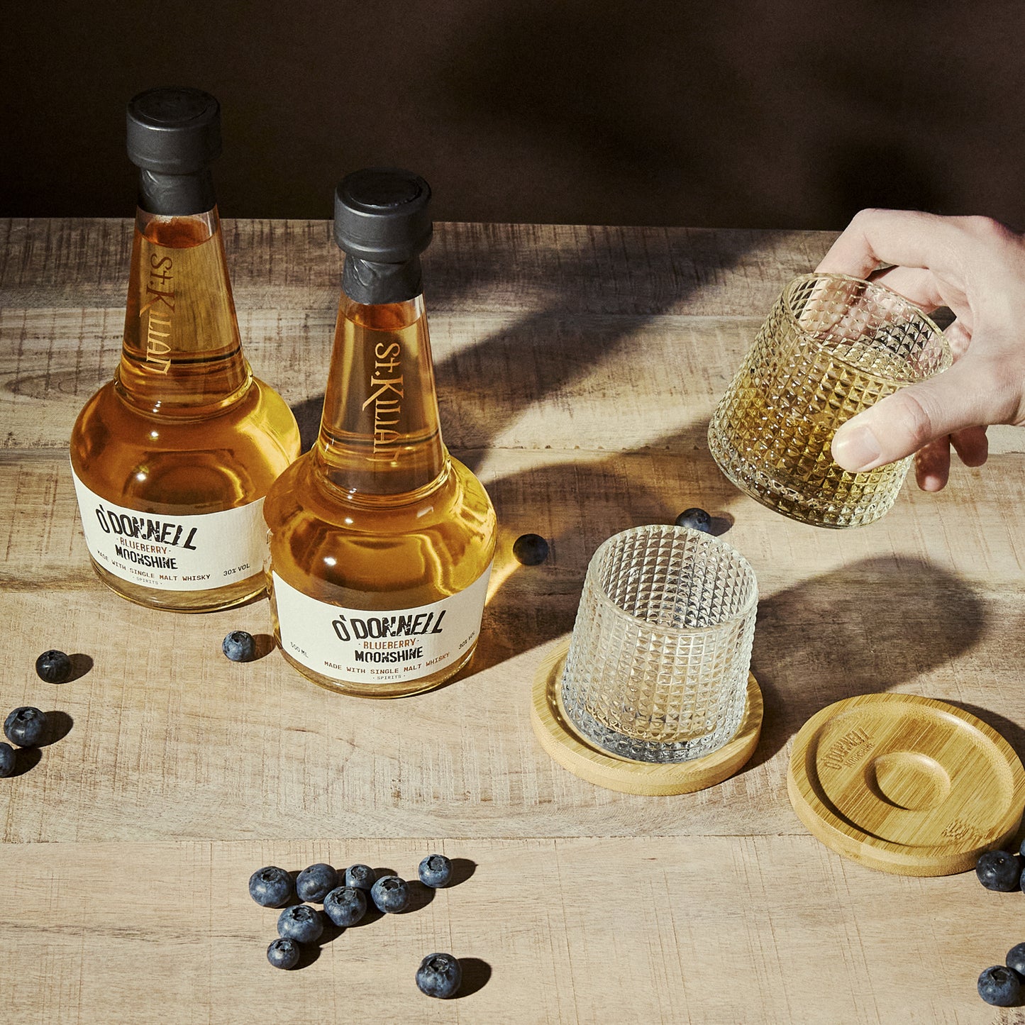 2 bottle of blueberry moonshine whisky with 2 glasses on a wooden surface