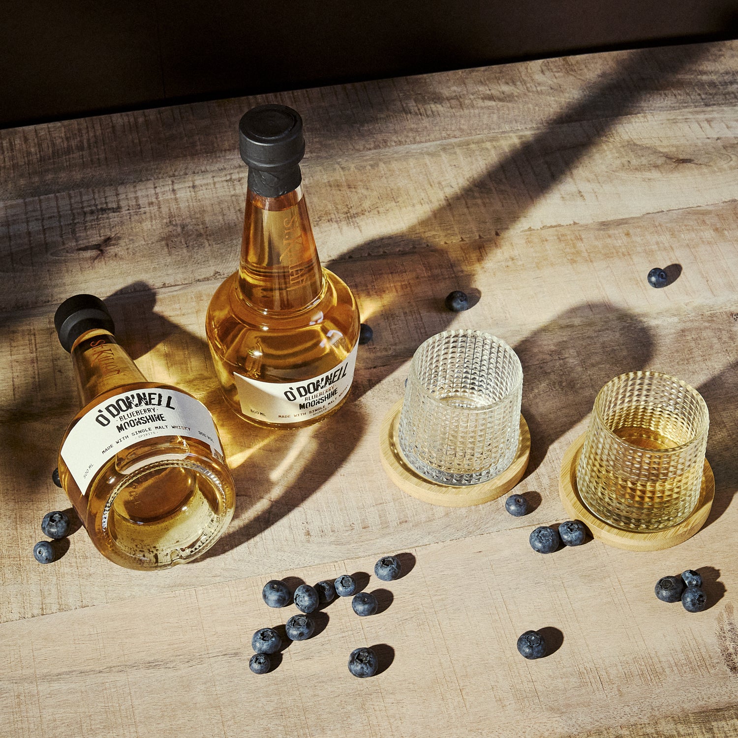 2 bottle of blueberry moonshine whisky with 2 glasses on a wooden surface