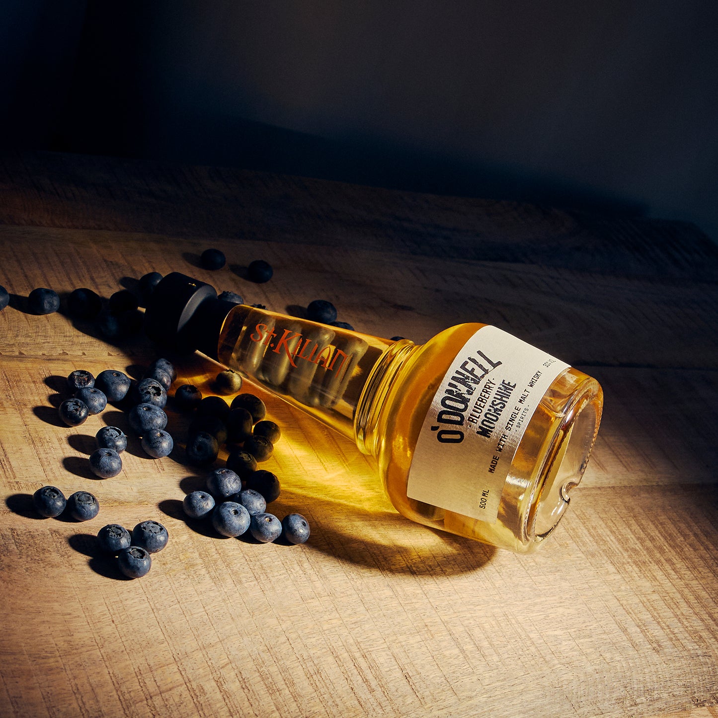 Blueberry Moonshine x Whiskey bottle on a wooden background surrounded by blueberries