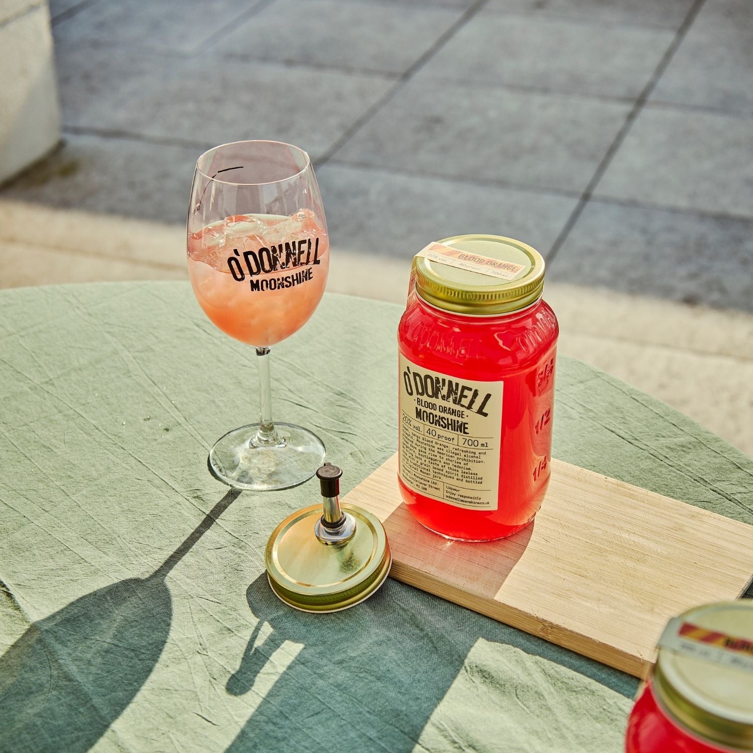 A blood Orange moonshine 700l Jar next to a O'Donnell Moonshine Spritz glass and a pouring lid.