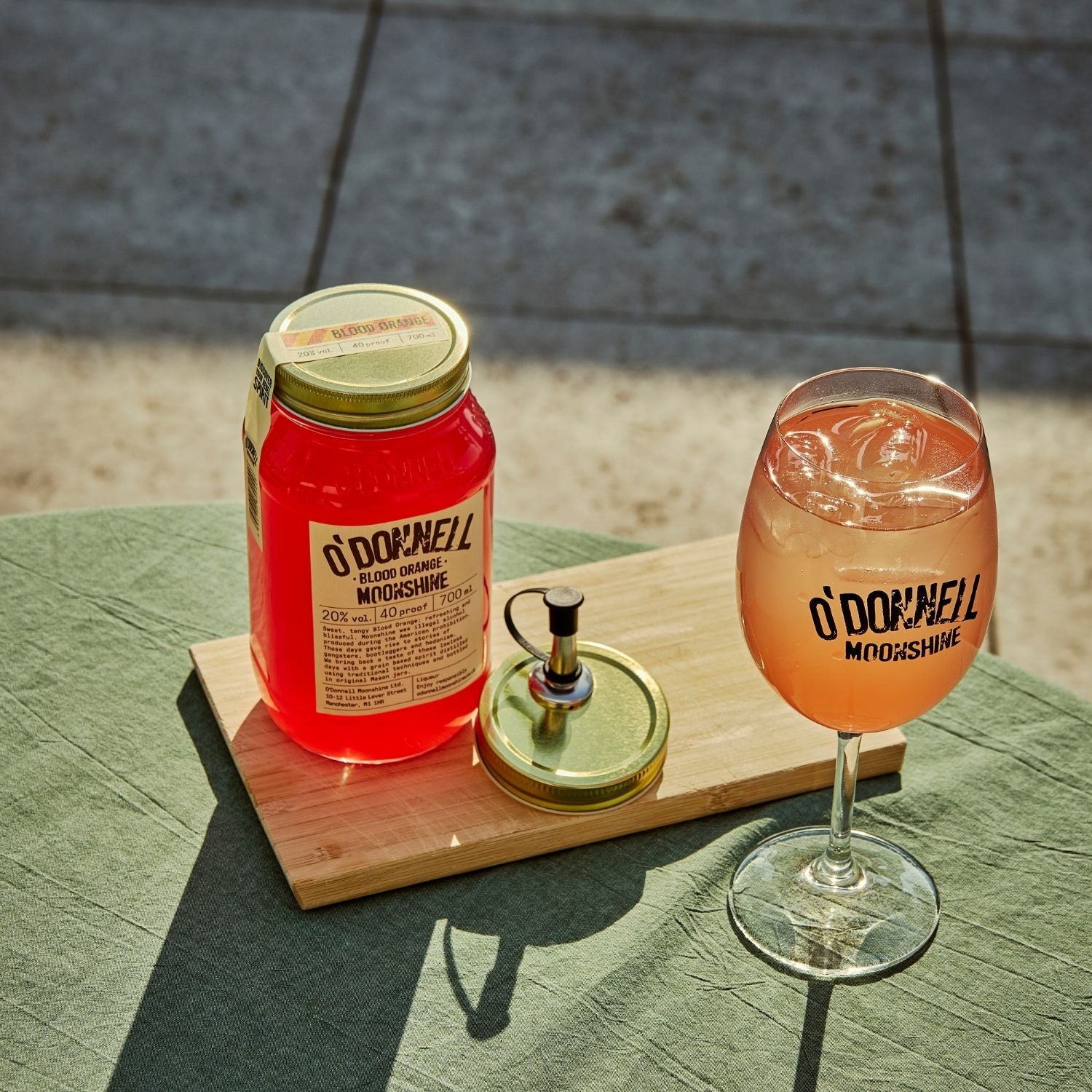 A blood Orange moonshine 700l Jar next to a O'Donnell Moonshine Spritz glass and a pouring lid.