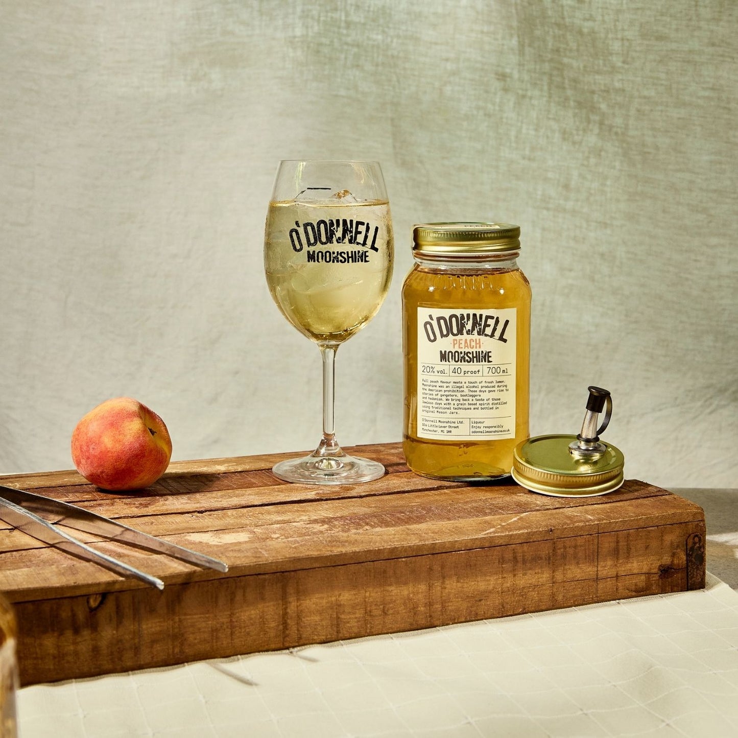A Peach moonshine 700l Jar next to a O'Donnell Moonshine Spritz glass and a pouring lid.