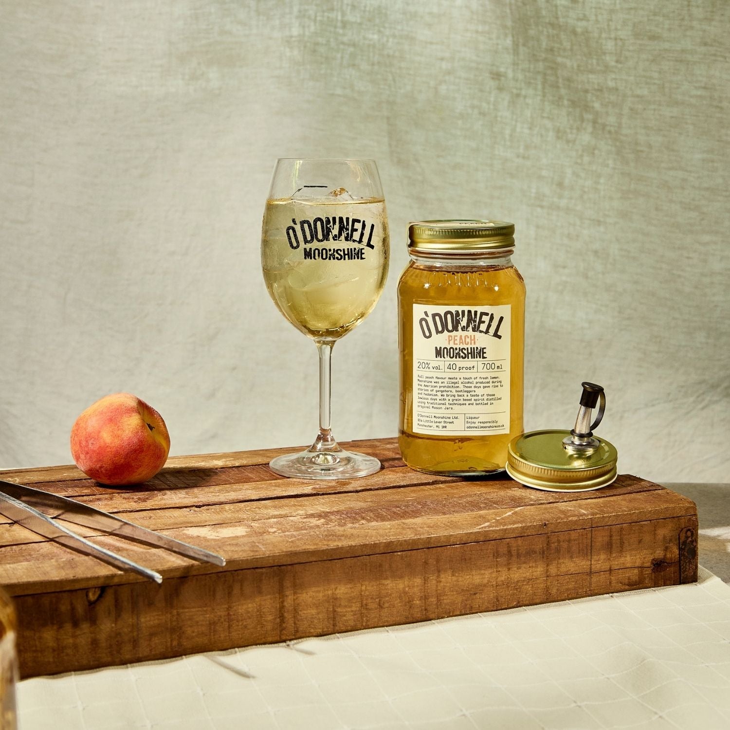 A Peach moonshine 700l Jar next to a O'Donnell Moonshine Spritz glass and a pouring lid.