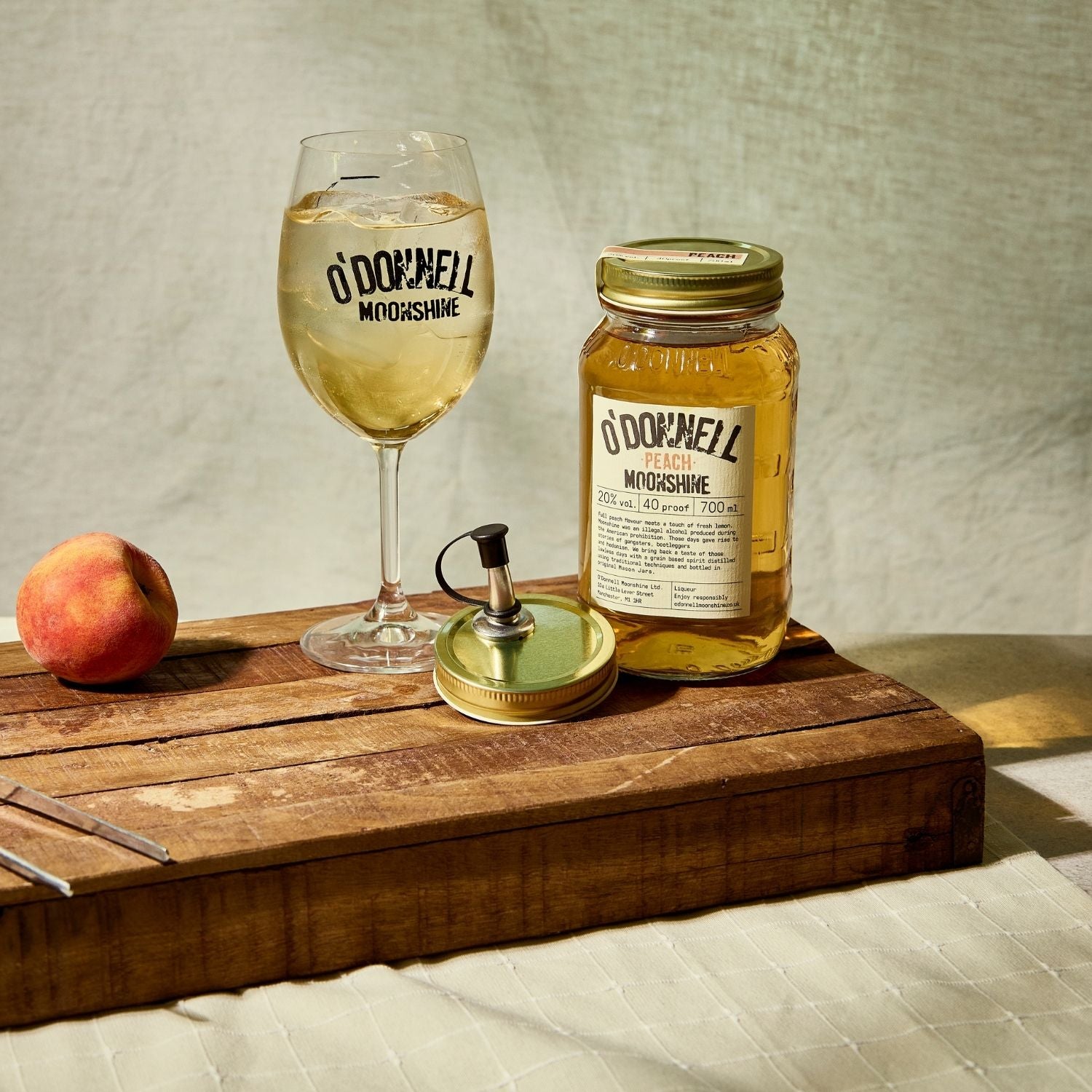 A Peach moonshine 700l Jar next to a O'Donnell Moonshine Spritz glass and a pouring lid.