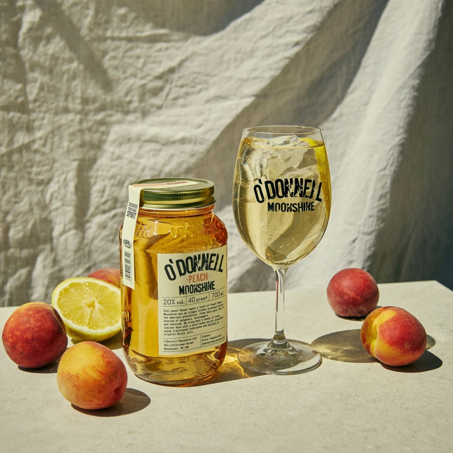 A Peach moonshine 700l Jar next to a O'Donnell Moonshine Spritz glass and a pouring lid.