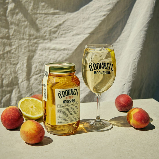 A Peach moonshine 700l Jar next to a O'Donnell Moonshine Spritz glass and a pouring lid.