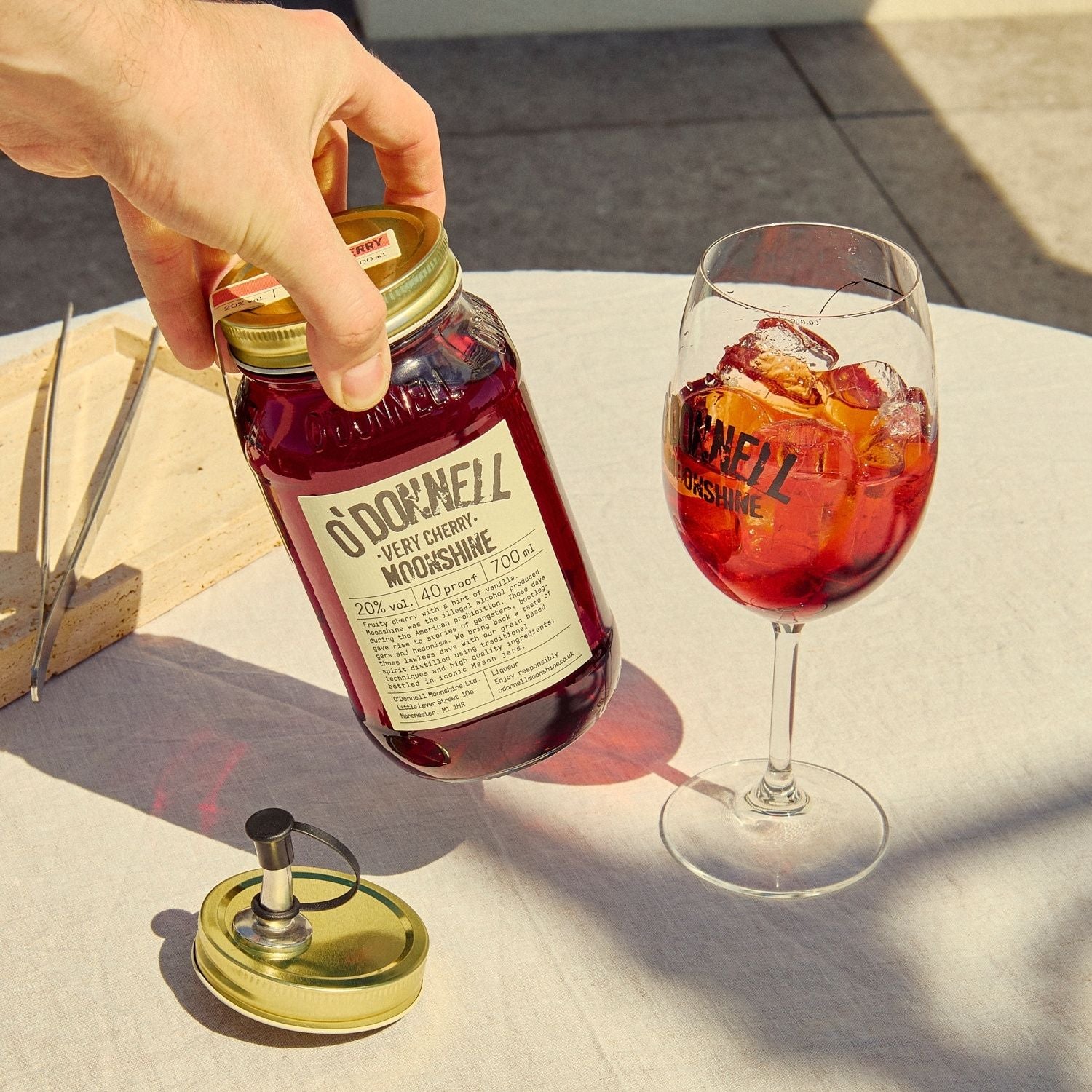 A Very Cherry moonshine 700l Jar next to a O'Donnell Moonshine Spritz glass and a pouring lid.