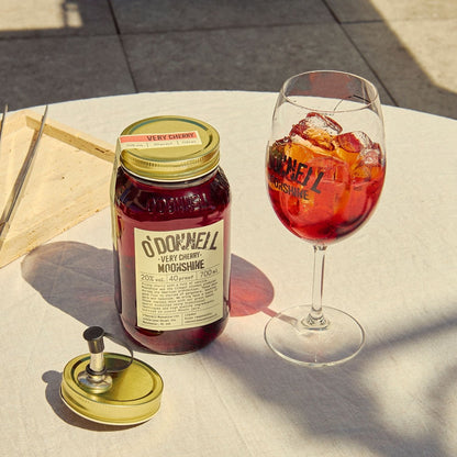 A Very Cherry moonshine 700l Jar next to a O'Donnell Moonshine Spritz glass and a pouring lid.