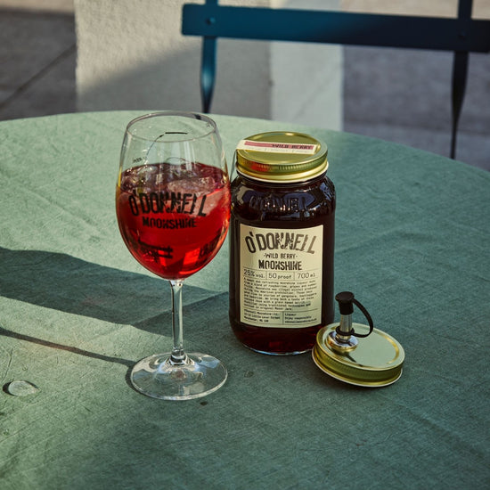 A Wild Berry moonshine 700l Jar next to a O'Donnell Moonshine Spritz glass and a pouring lid.