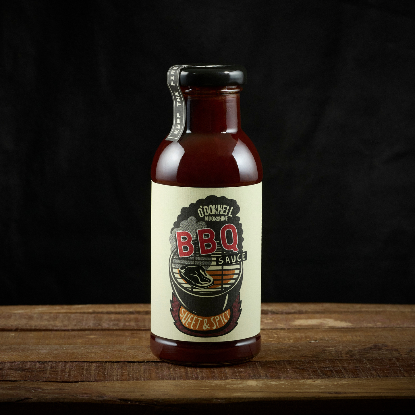 Bottle of BBQ sauce with a label on a wooden surface and black background