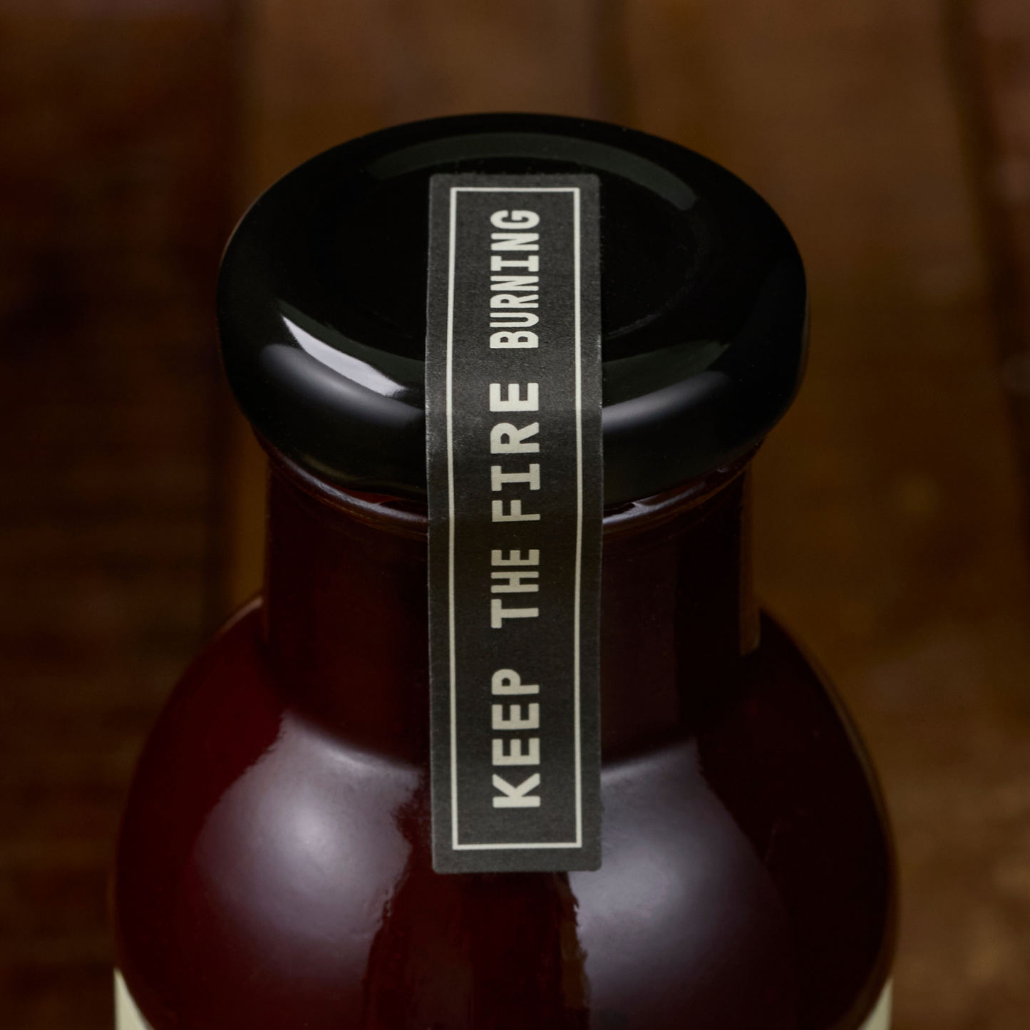 Bottle with a black cap and 'Keep the Fire Burning' label on a wooden background