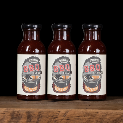 Three bottles of O'Donnell BBQ Sauce on a wooden surface with a black background