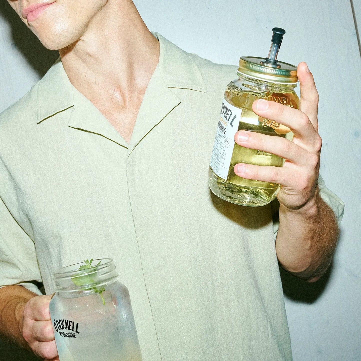 O'Donnell Moonshine Elderflower Liqueur in a Mason jar, with a man in the foreground enjoying it as a cocktail.