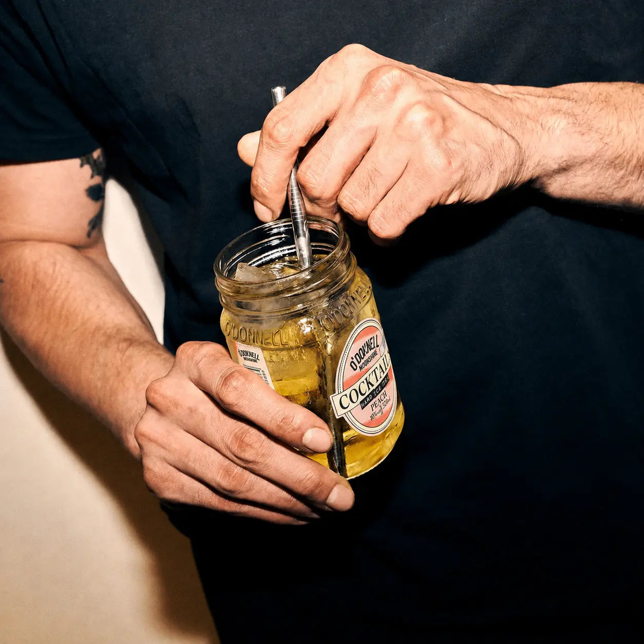 Person opening a jar of pickles with a spoon against a dark background