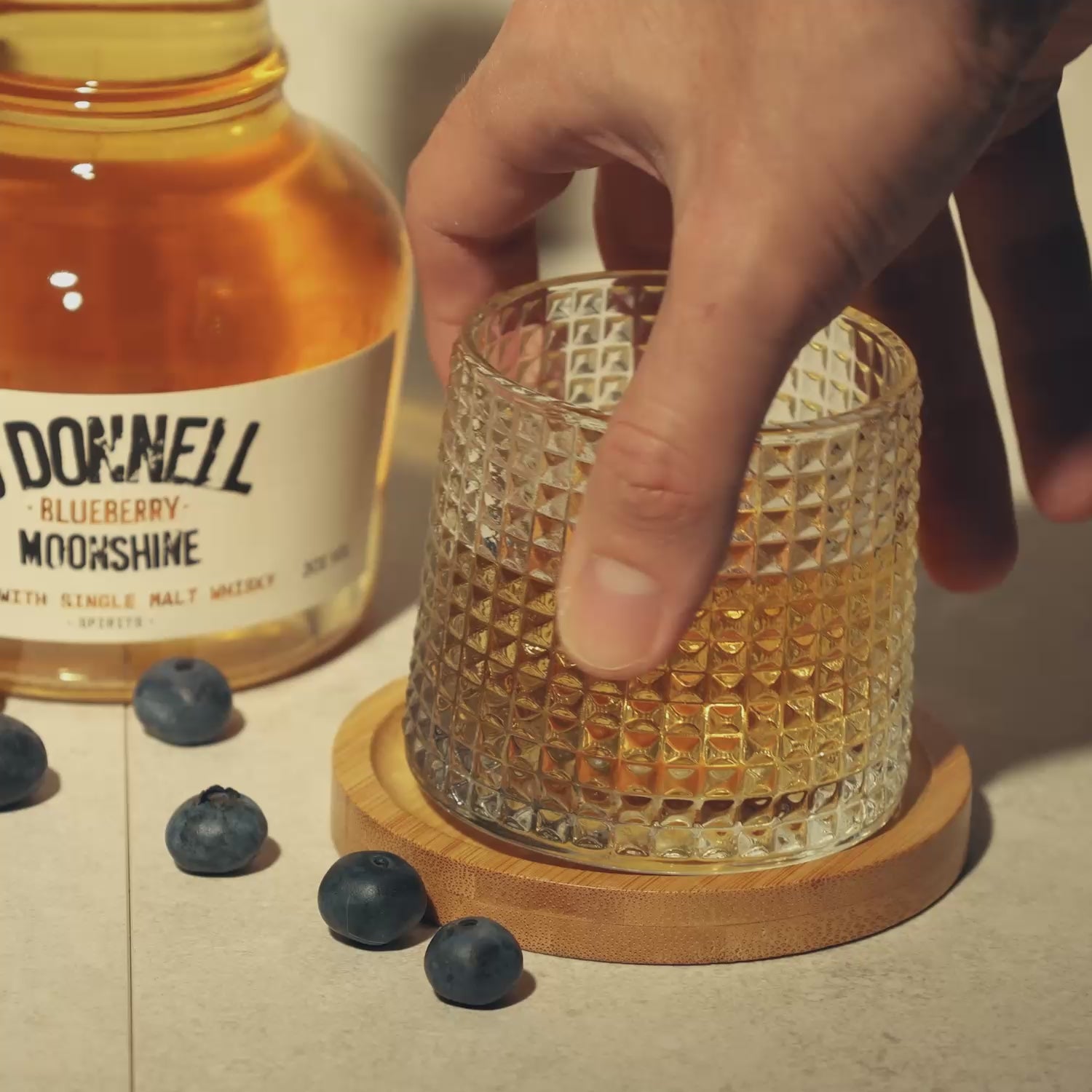 Textured Tumbler Glass on a wooden coaster. Surrounded by blueberries being spun round
